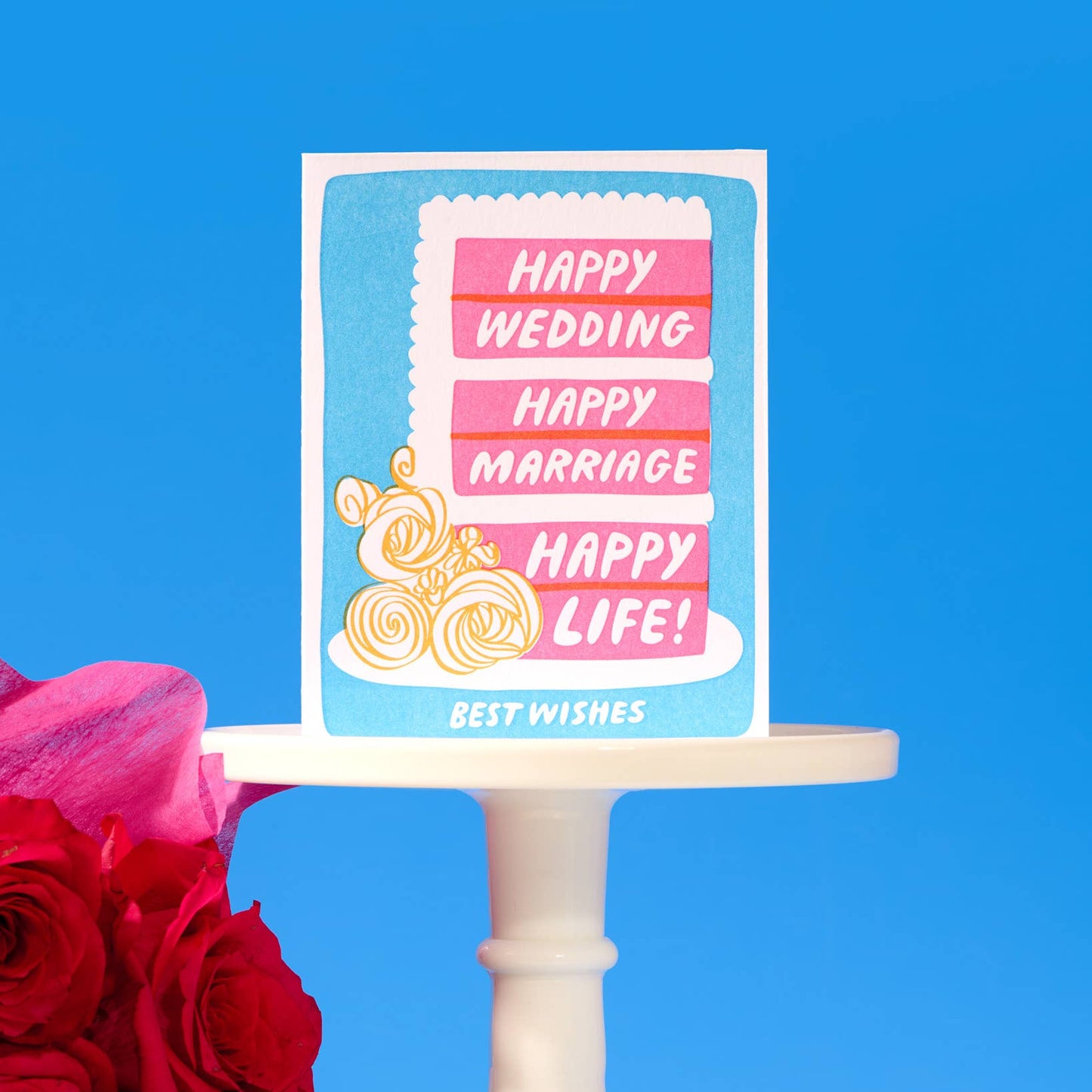 Card with 'Happy Wedding, Happy Marriage, Happy Life!' text on a cake stand with flowers against a blue background