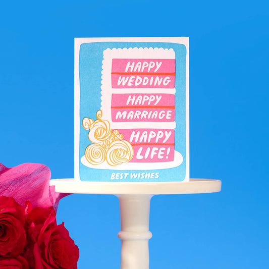 Card with 'Happy Wedding, Happy Marriage, Happy Life!' text on a cake stand with flowers against a blue background