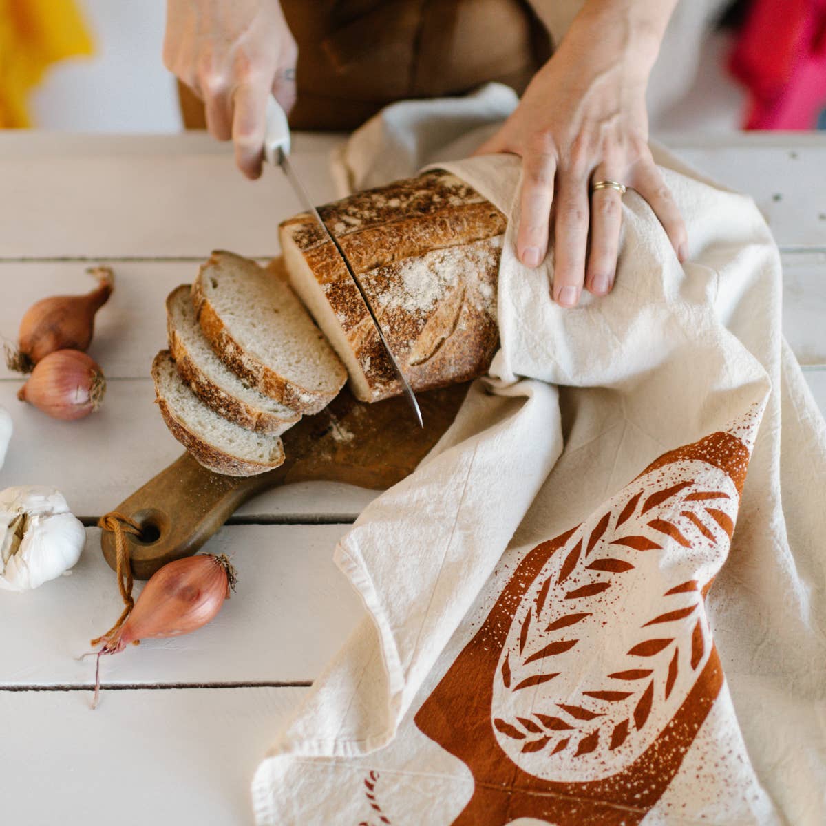 kitchen towel designed with a loaf of bread on a bread board being used to hold a loaf of bread while being cut into