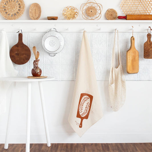 kitchen towel designed with a loaf of bread on a bread board hanging on a peg 