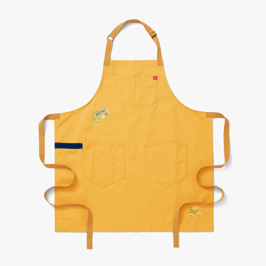 Egg yolk colored apron with gold and navy straps featuring two pops of embroidery: butter in its iconic paper wrapping at the waist and a pat of melting rich and creamy butter at the hem