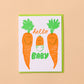 Card with cartoon carrots, 2 regular and one baby, and text 'hello baby' on a beige background