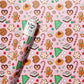 Wrapping paper roll with a pink background and Christmas-themed cookies and candies.
