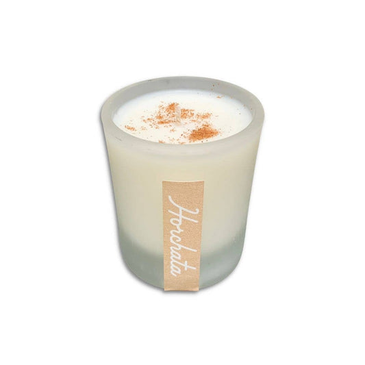 White candle in frosted glass with a sprinkle of cinnamon on top, labeled with "Horchata" on a white background