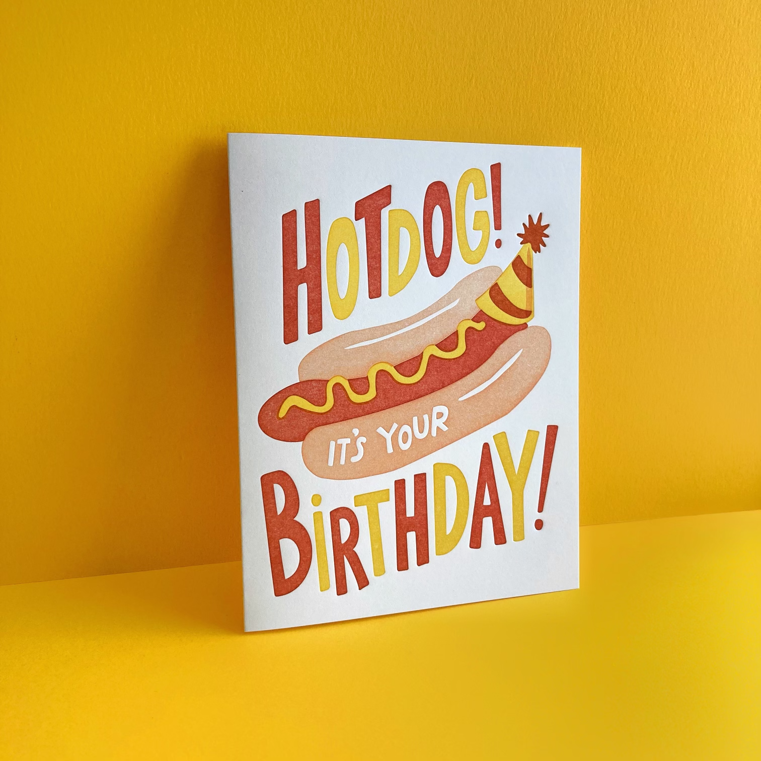 Greeting card with a yellow envelope -- text reads "Hotdog! it's your birthday!" with an image of a hot dog in a bun with mustard on it, wearing a birthday party hat