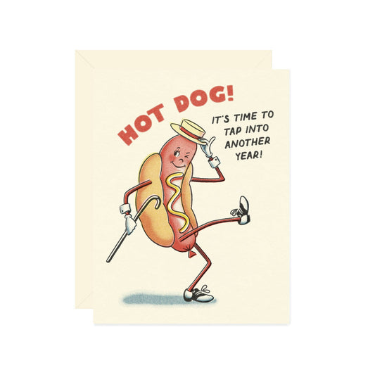 Card with a cartoon hot dog character tap dancing and text "hot dog! it's time to tap into another year!" on a beige background