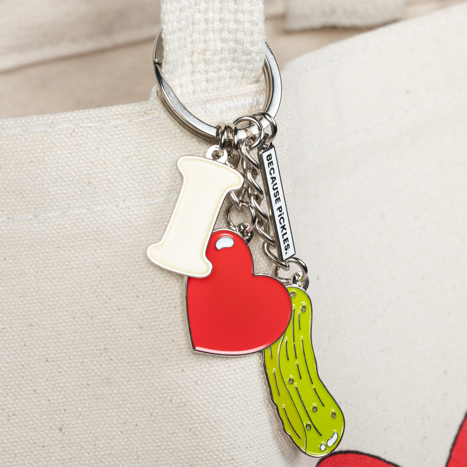 Keychain with heart, pickle, and letter "i" charms on a beige background