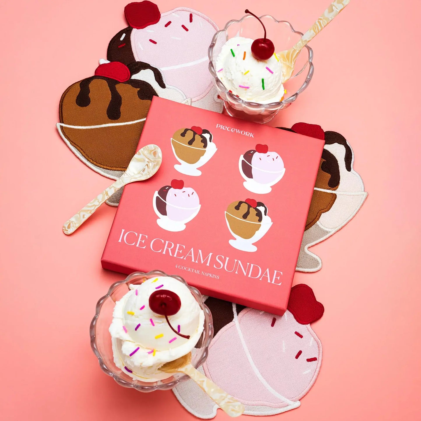 Pink box with ice cream sundae design surrounded by ice cream sundae shaped cocktail napkins on a pink background