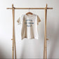Beige t-shirt with 'Official Ice Cream Taster' text on a wooden rack against a white background