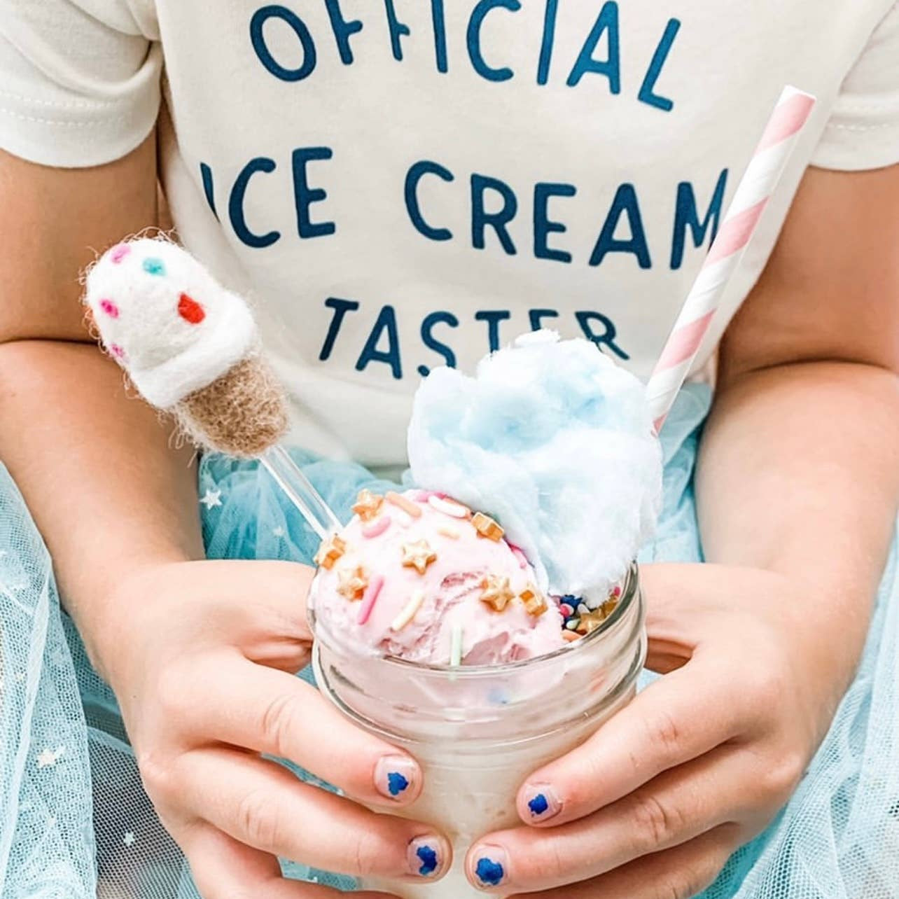 Child holding a colorful ice cream shake with a straw, wearing a shirt that says 'Official Ice Cream Taster'.