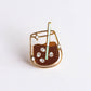 Enamel pin of a glass of iced coffee with a straw on a white background