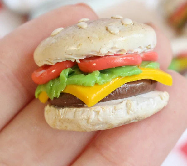 Close-up photo of a single tiny cheeseburger magnet resting on the tips of a person's fingers.