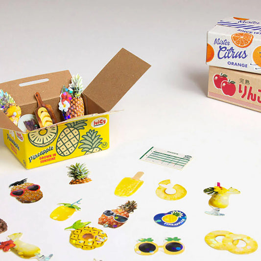 Open box with pineapple-themed stickers on a light gray background