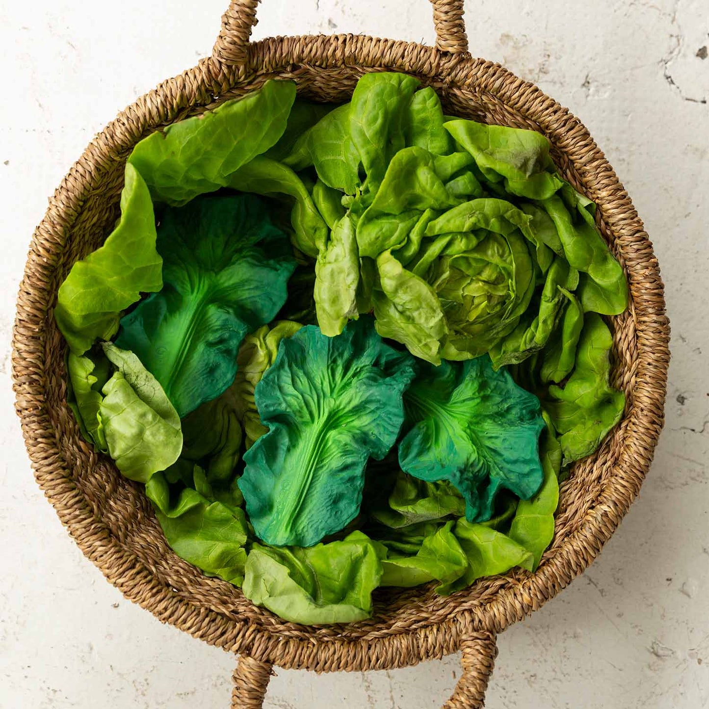 Photo of three kale baby toys lying on top of a basket full of real lettuce.