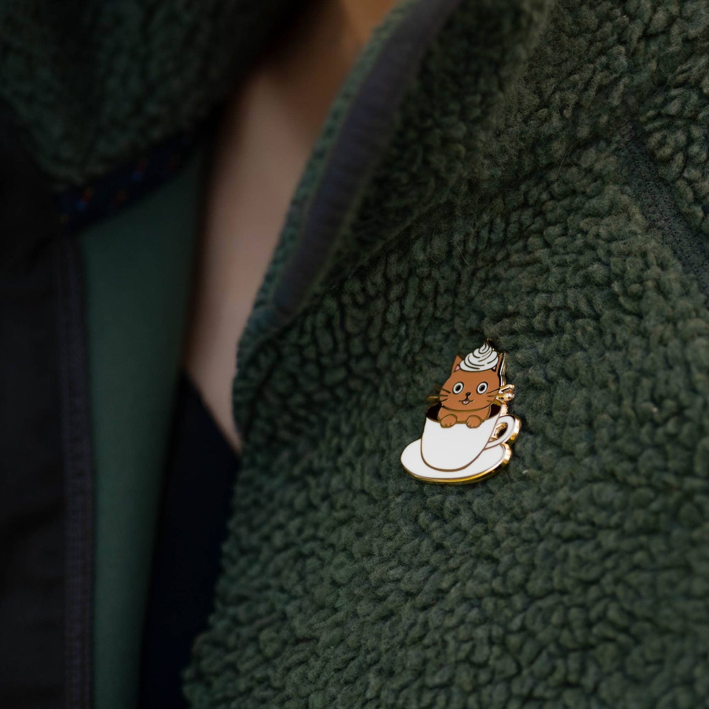 Cat-themed pin on a green fleece jacket