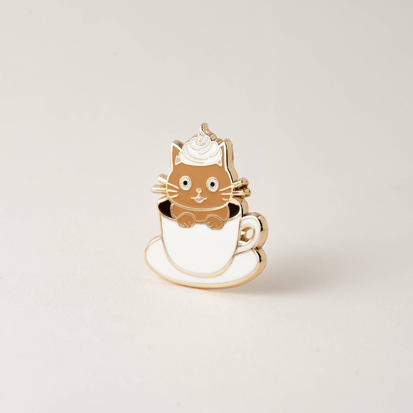 Cat-shaped pin in a tea/coffee cup on a beige background