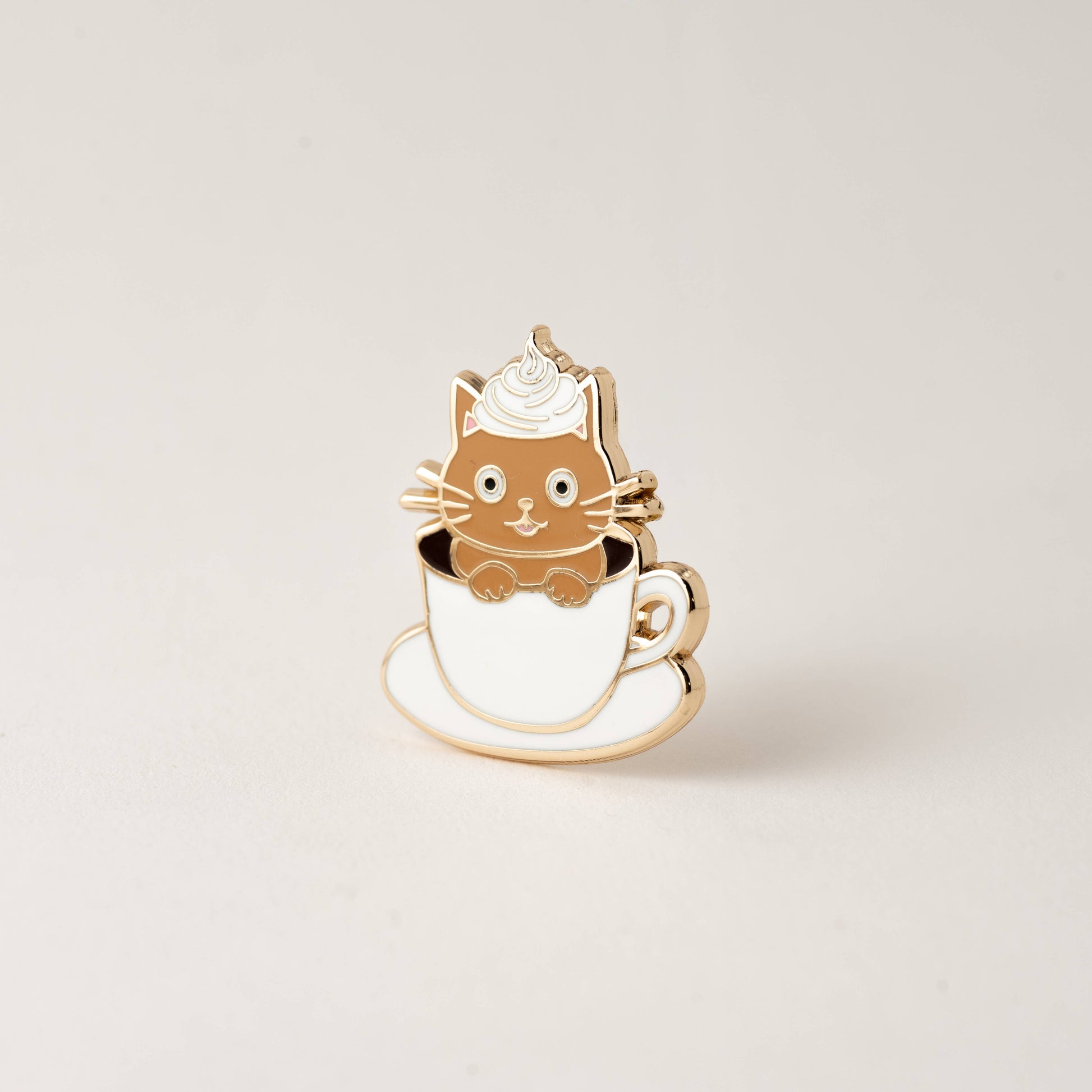 Cat-shaped pin in a tea/coffee cup on a beige background