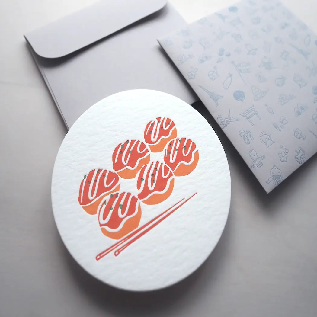 round notecard with takoyaki design. Envelope is light grey with various illustrations of notable landmarks, attractions, food and drink from Japan