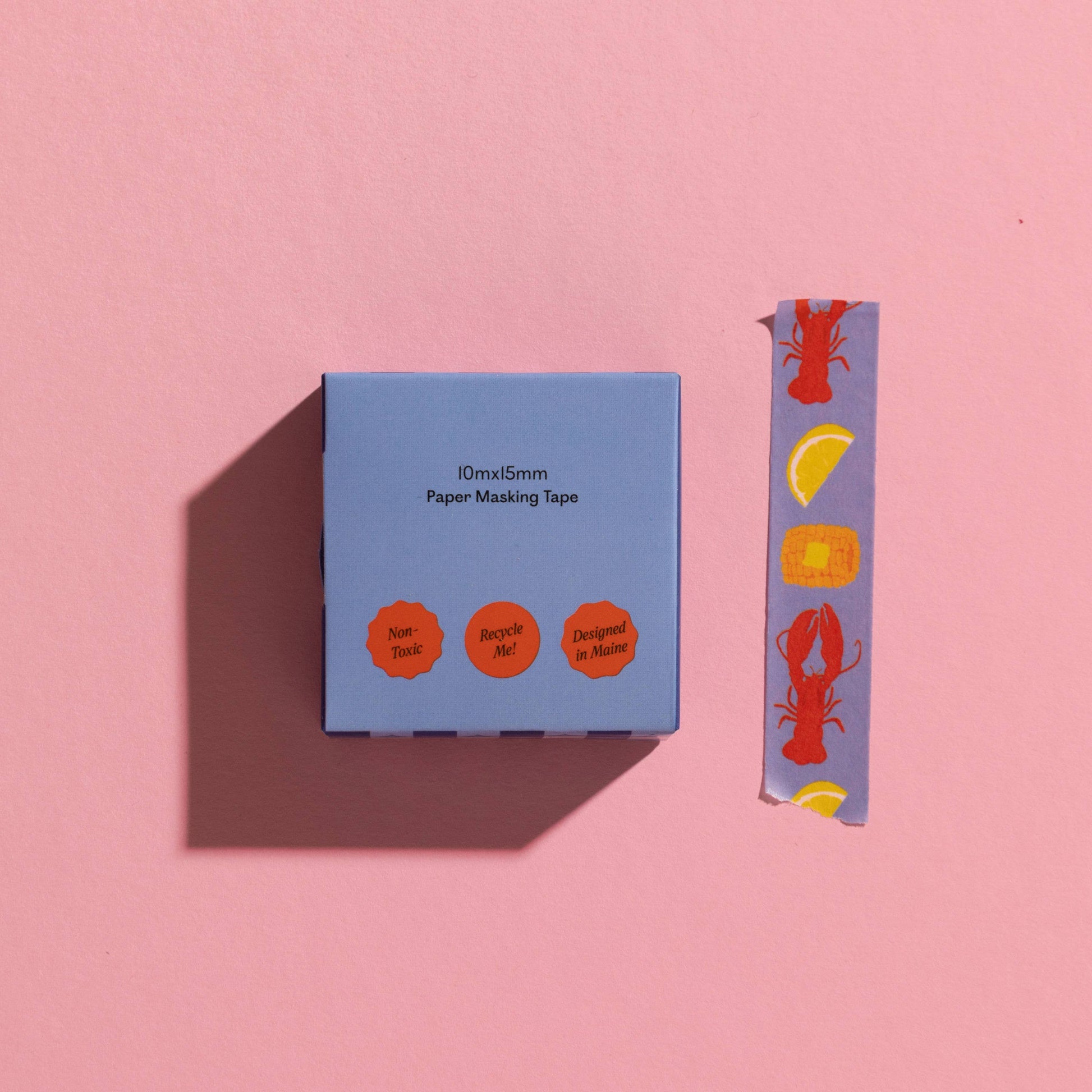 Blue washi tape box with a strip of decorative tape on a pink background