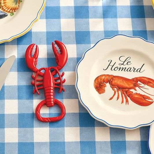 Red lobster-shaped bottle opener on a blue and white checkered tablecloth with a plate featuring a lobster design.