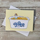Greeting card with woman sitting in a mac and cheese filled vintage corningware dish