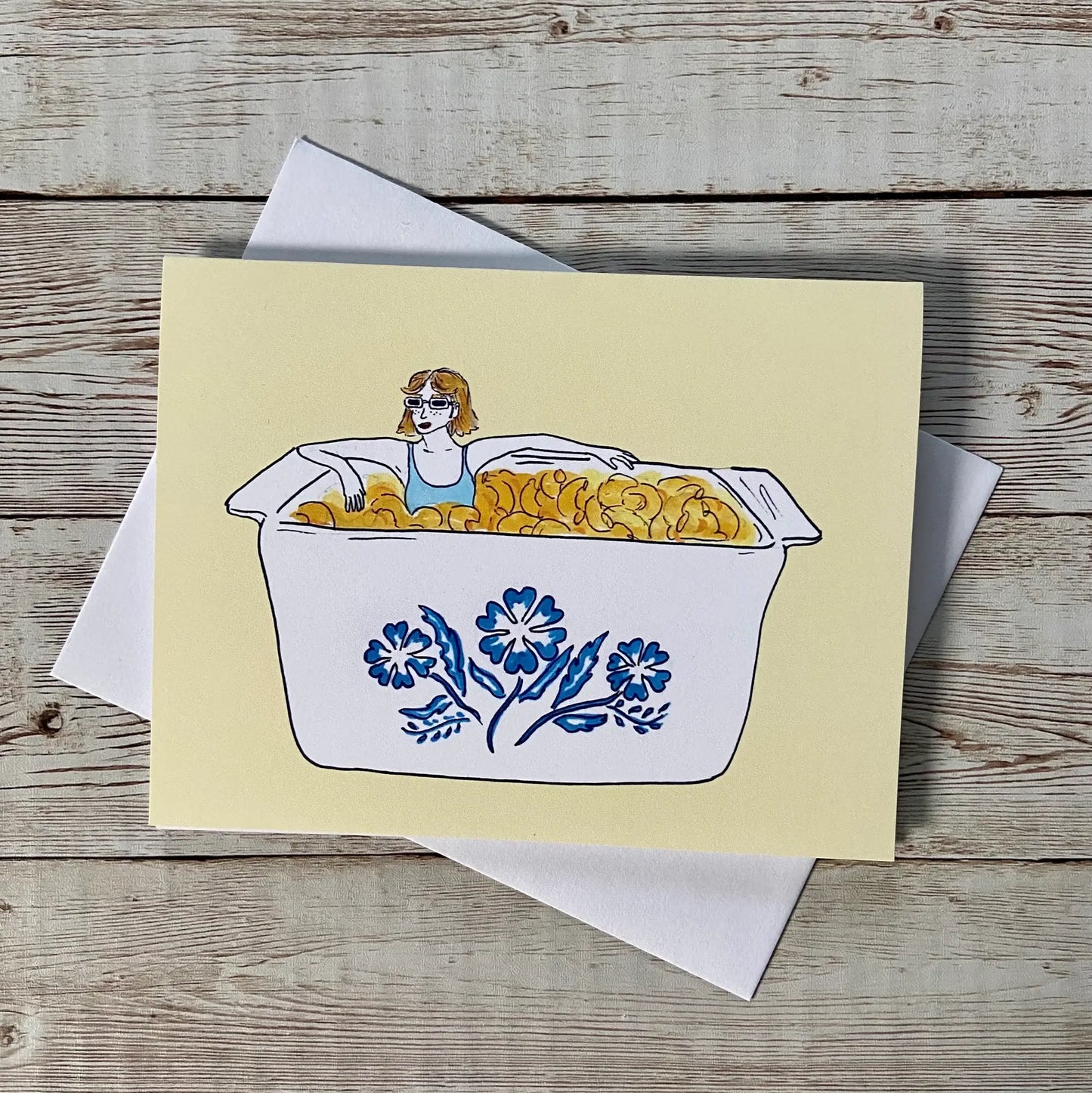 Greeting card with woman sitting in a mac and cheese filled vintage corningware dish