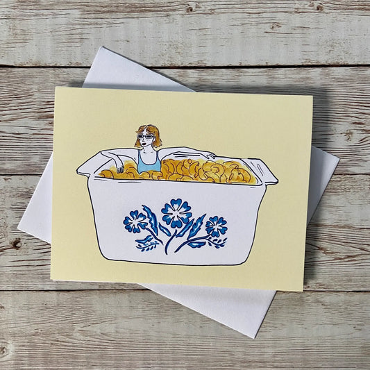 Greeting card with woman sitting in a mac and cheese filled vintage corningware dish