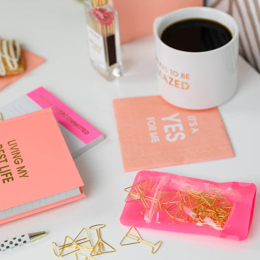 Desk with coffee mug, pink notebook, and decorative items, including the martini glass shaped paper clips, on a white surface