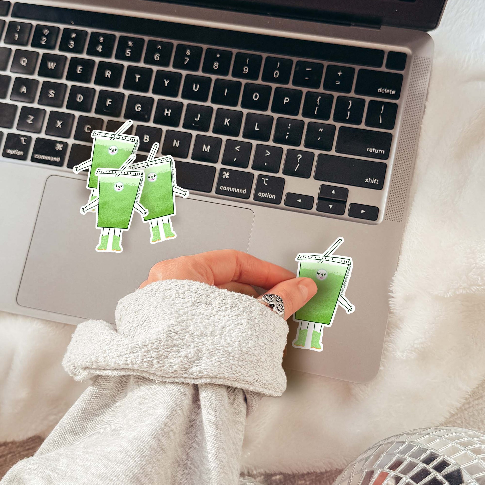sticker of a cartoon iced matcha character being put on a laptop