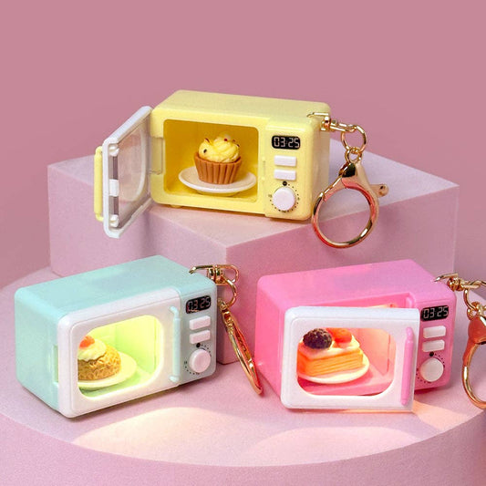 Set of three colorful microwave-shaped keychains with digital displays and small cakes inside on a pink background.