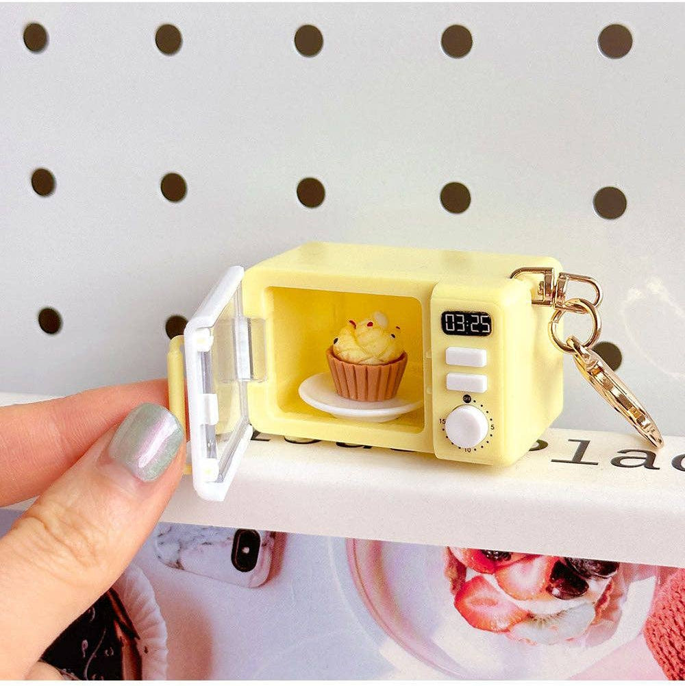 Yellow microwave-shaped keychain with a cupcake inside, held by a hand.
