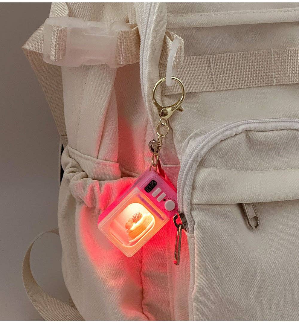 Mini microwave keychain lit up and attached to a beige backpack