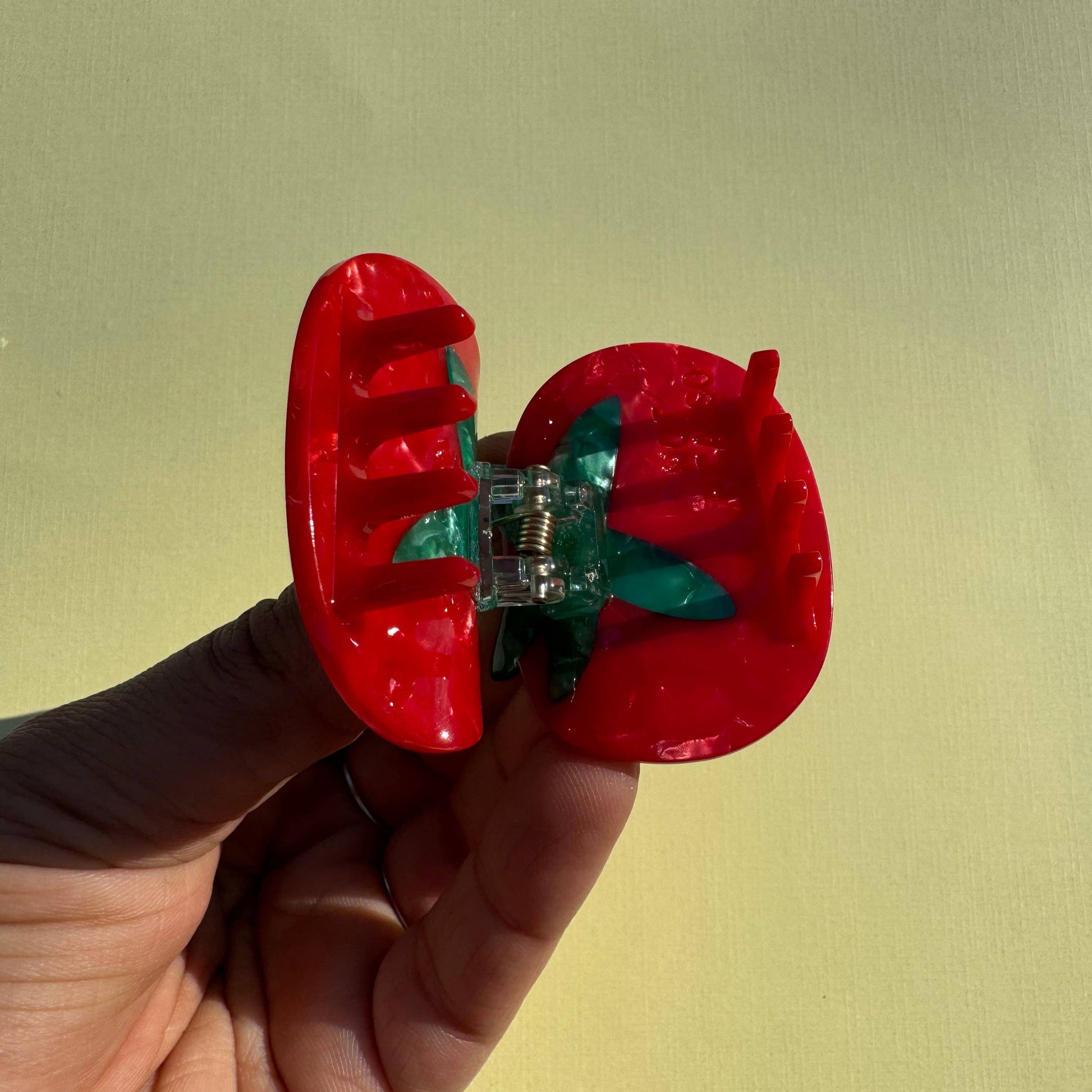 Red tomato-shaped mini hair claw with a clear center held by a hand against a yellow background
