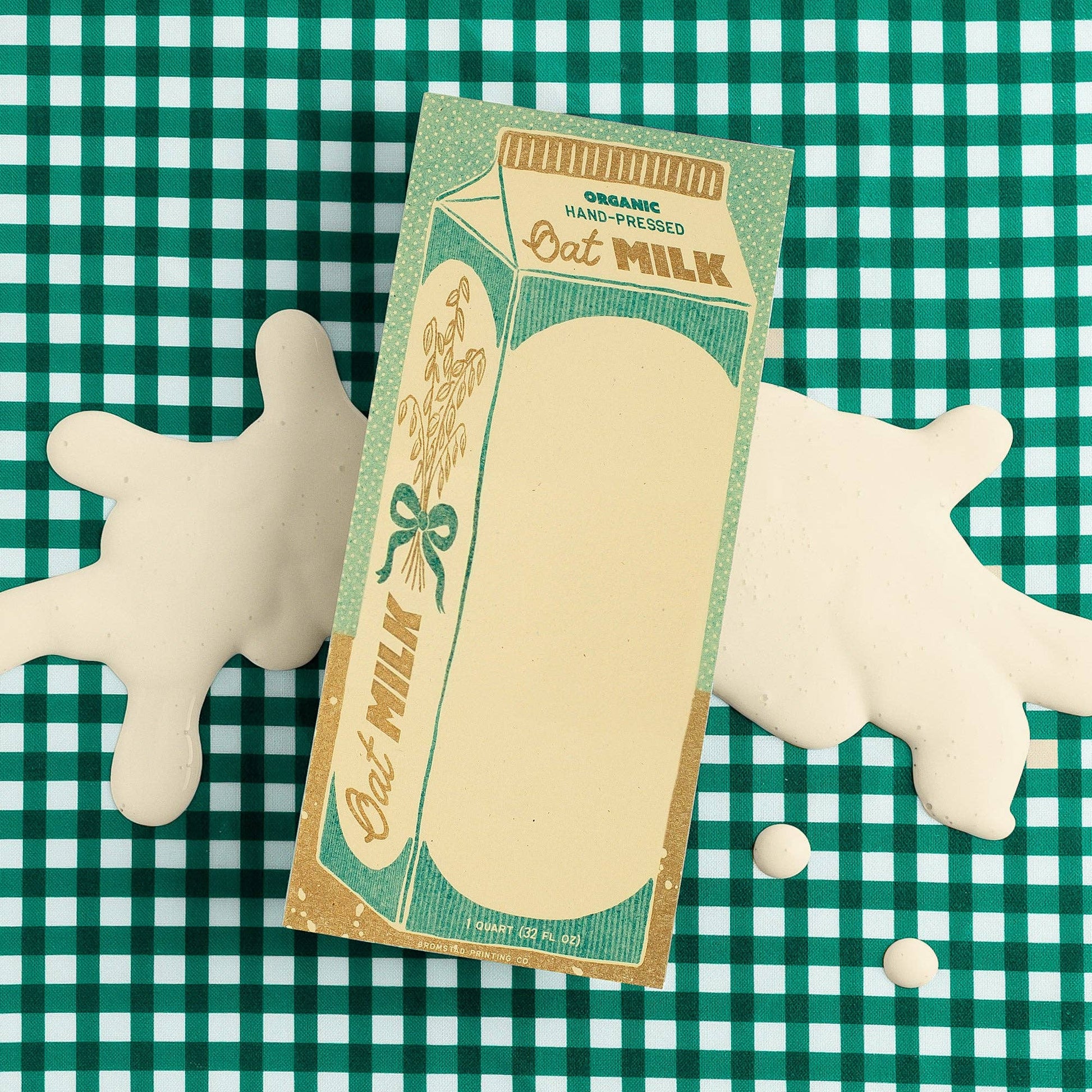 Notepad designed to look like an oat milk carton pictured on a teal and white checkerboard background 