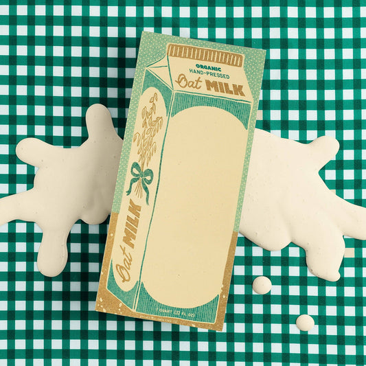 Notepad designed to look like an oat milk carton pictured on a teal and white checkerboard background 