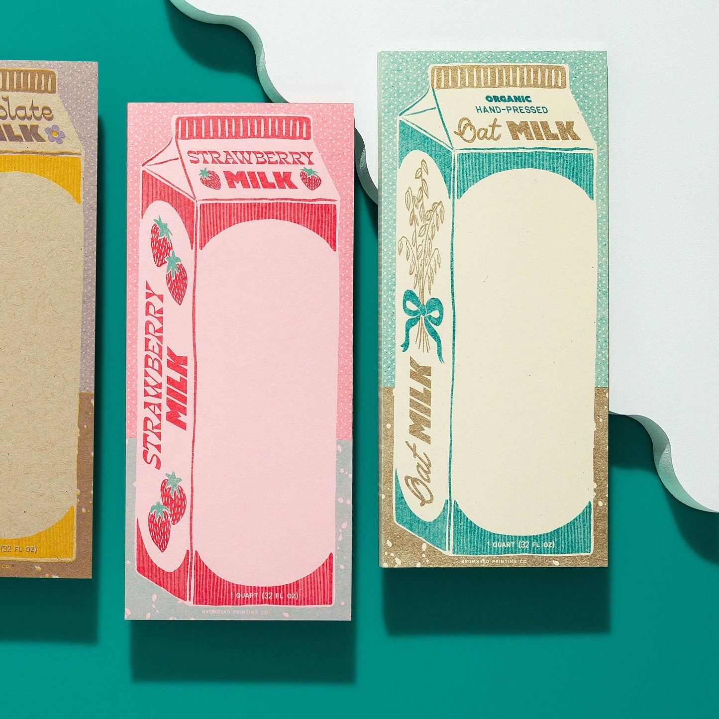 Three colorful milk carton-shaped notepads (chocolate, strawberry and oat) on a teal background