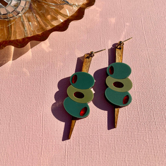 3 Green olives on a pick earrings with gold accents on a pink surface