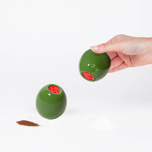 Stuffed green olive shaped salt and pepper shakers held by a hand on a white background