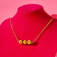 Necklace with gold chain and set of 3 stuffed green olive charms on a red mannequin against a pink background