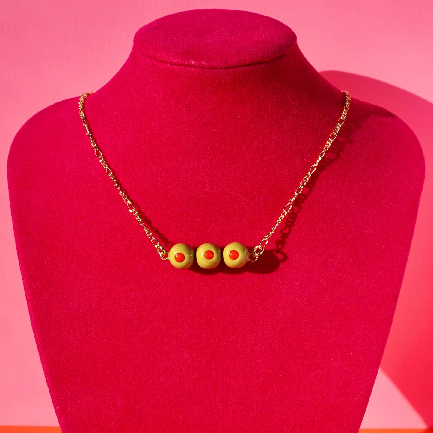 Necklace with 3 stuffed green olive charms on a red mannequin against a pink background