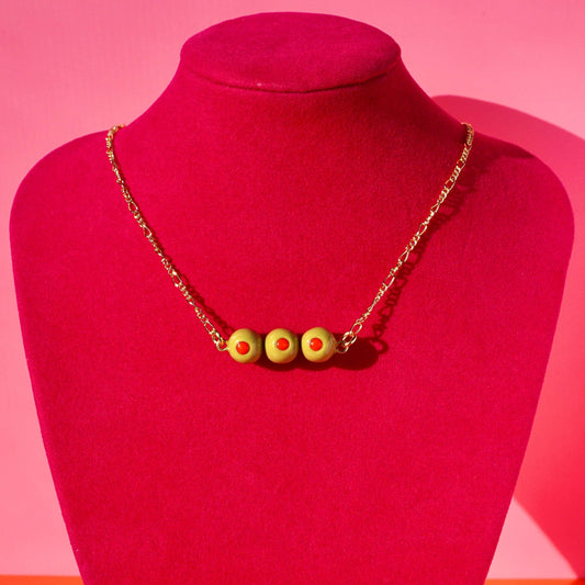 Necklace with 3 stuffed green olive charms on a red mannequin against a pink background