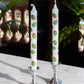 Two candles with stuffed green olive design in silver candle holders on a marble surface with a blurred natural background.