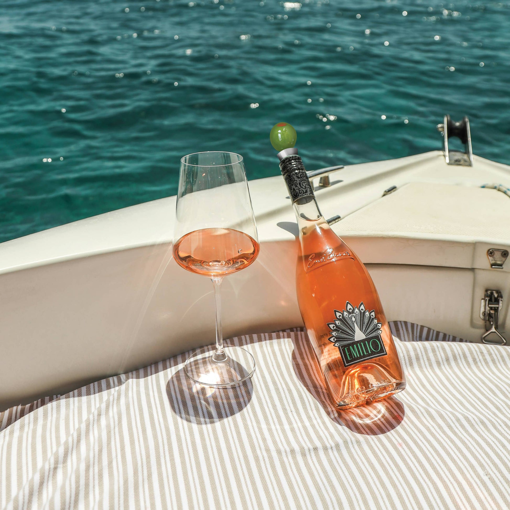 Bottle of Fiano wine, with the olive wine stopper in it and a glass on a boat with ocean view