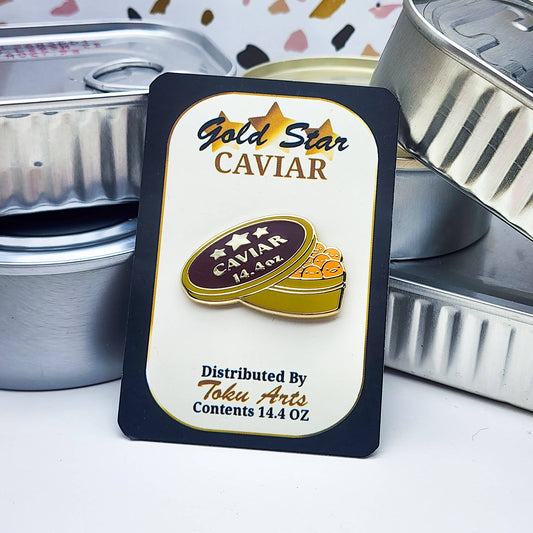 Gold Star Caviar packaging for the caviar enamel pin with orange fish eggs, with tinned fish containers in the background