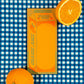 Carton of orange juice illustration on rectangular notepad with a sliced orange on a blue and white checkered background