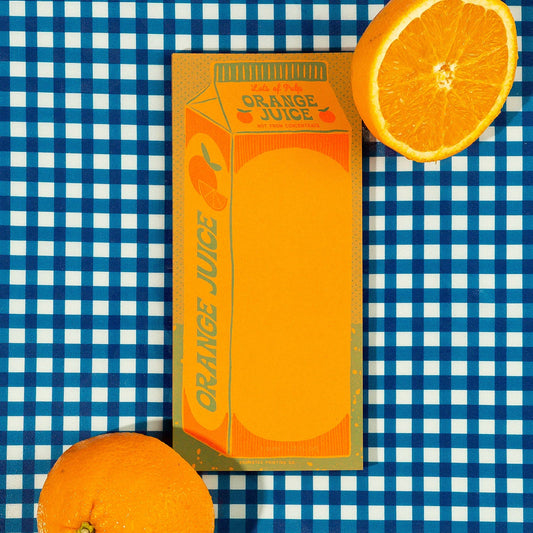 Carton of orange juice illustration on rectangular notepad with a sliced orange on a blue and white checkered background