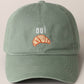 A green baseball cap with 'oui' written on it and an embroidered croissant below the text.