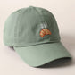 A green baseball cap with 'oui' written on it and an embroidered croissant below the text.
