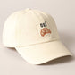 A cream baseball cap with 'oui' written on it and an embroidered croissant below the text.