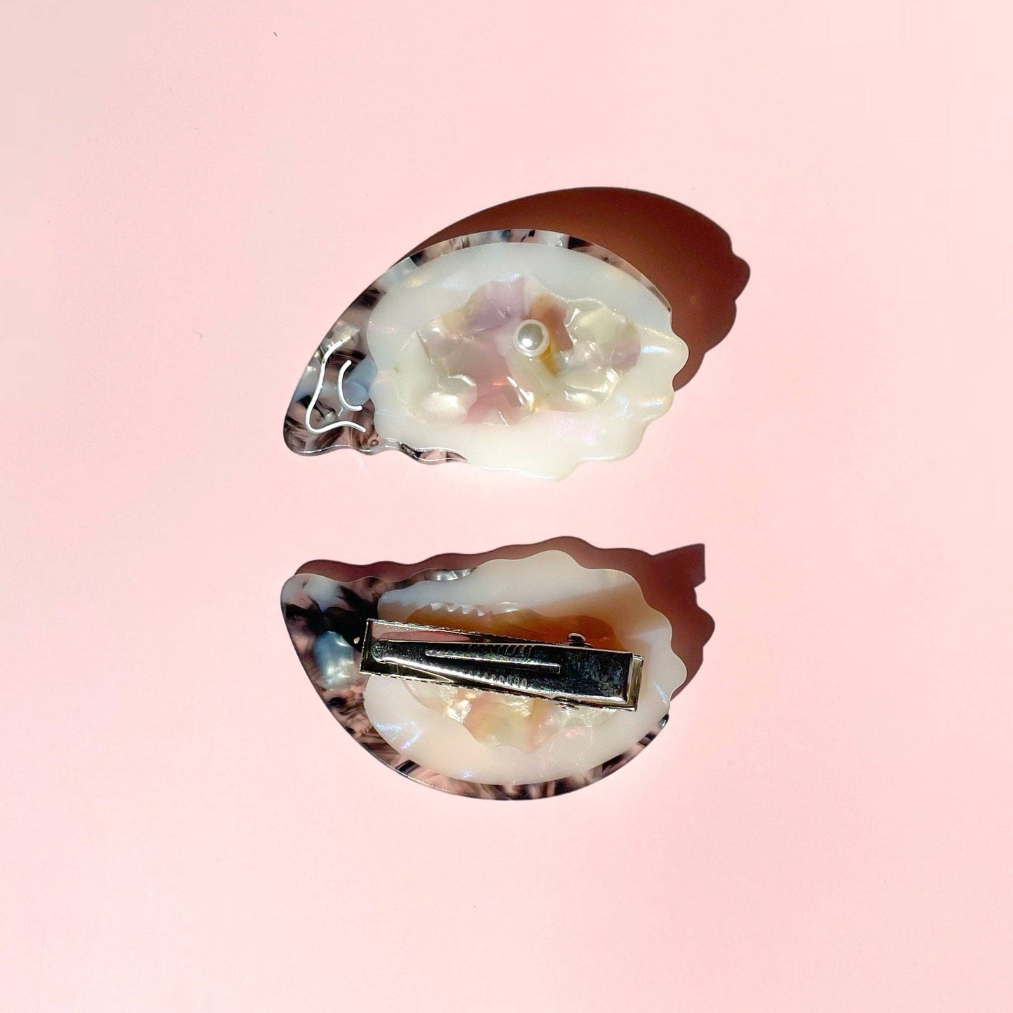 Oyster-shaped hair clips with pearlescent design on a pink background